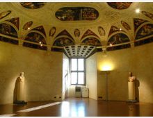 Sala interna con grande finestra centrale e pareti intonacate, pavimento lucido e due busti su piedistalli ai lati. Il soffitto è a volta con ricche decorazioni e riquadri affrescati, illuminato da faretti.